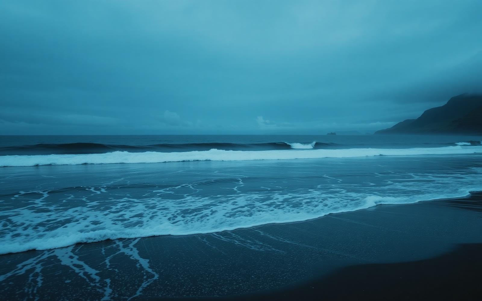Waves rolling onto a quiet Scottish shore at dusk under a deep blue sky.